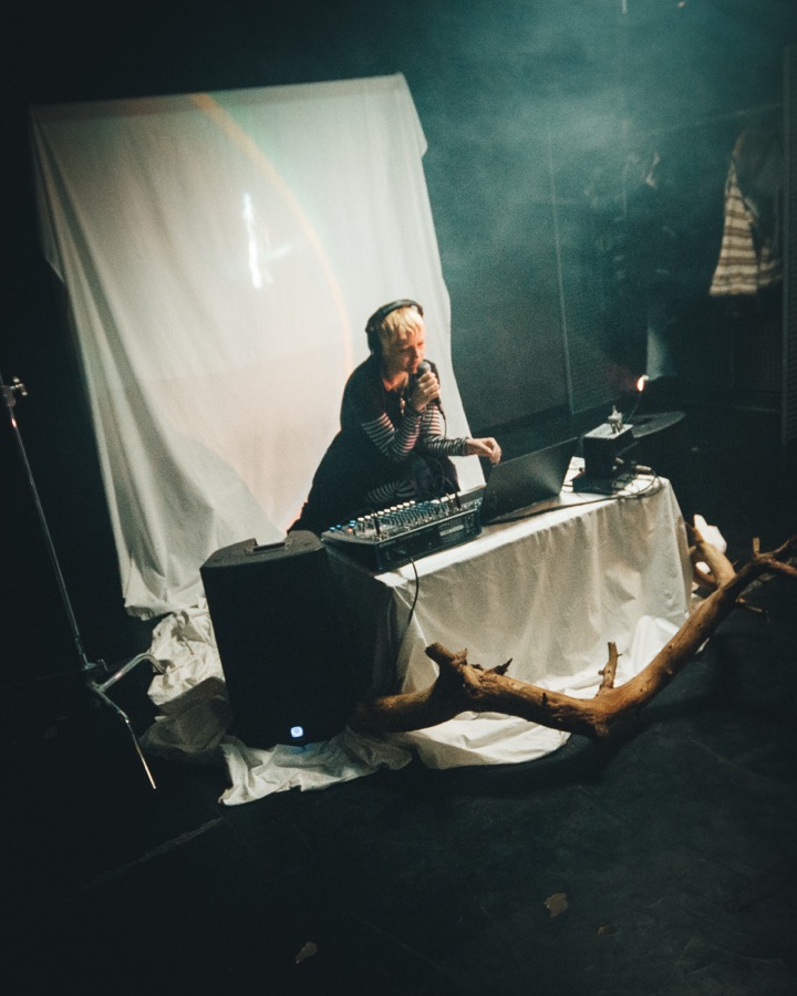DJ playing in haze in front of a draped white backdrop, with driftwood from the set