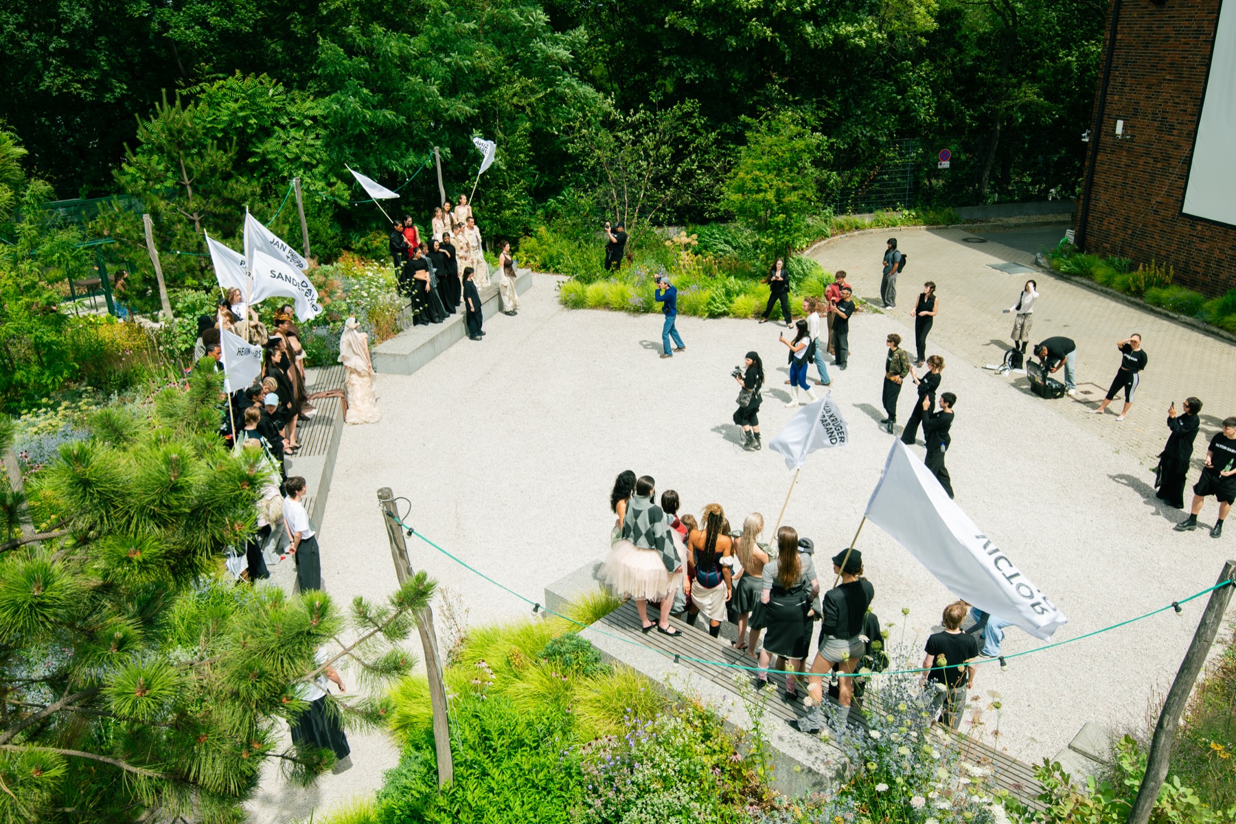 Aerial view of the LETTE SS27 garden runway at Atelier Gardens, models carrying white flags through the greenery